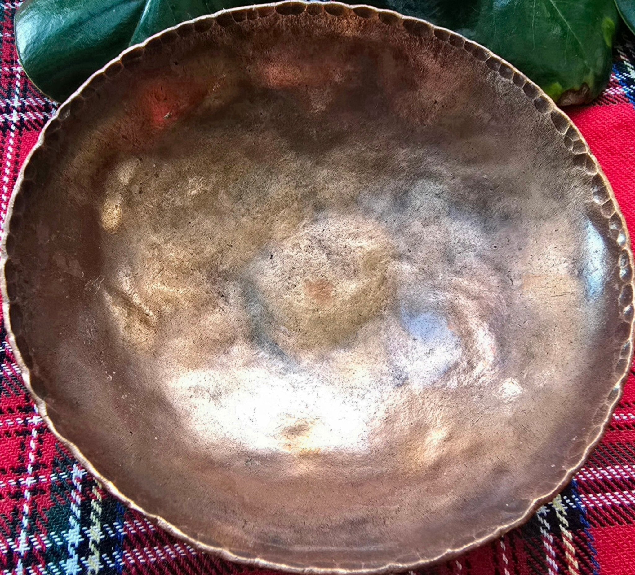 Rustic hammered copper bowl on plaid fabric. Handmade decorative bowl for fruit or display.