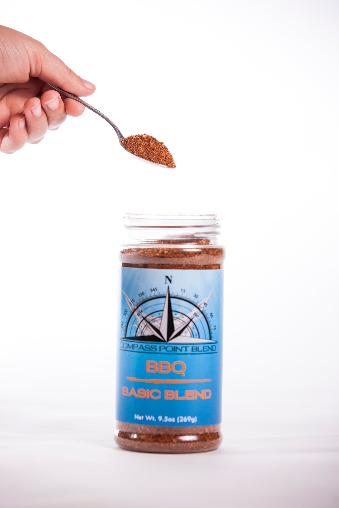Compass Point BBQ Basic Blend Seasoning: Hand with spoon pouring BBQ blend seasoning in the jar.