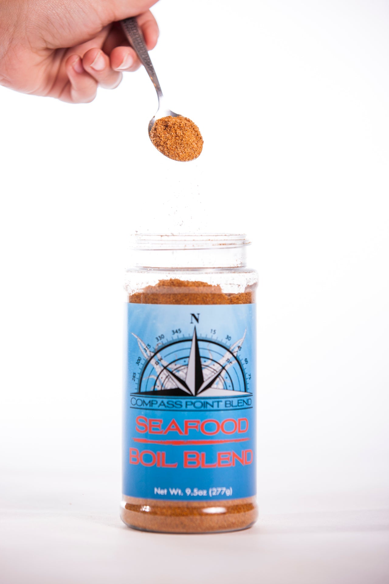 Seafood Boil Blend: Compass Point Blend being poured into container with spice on spoon over jar.
