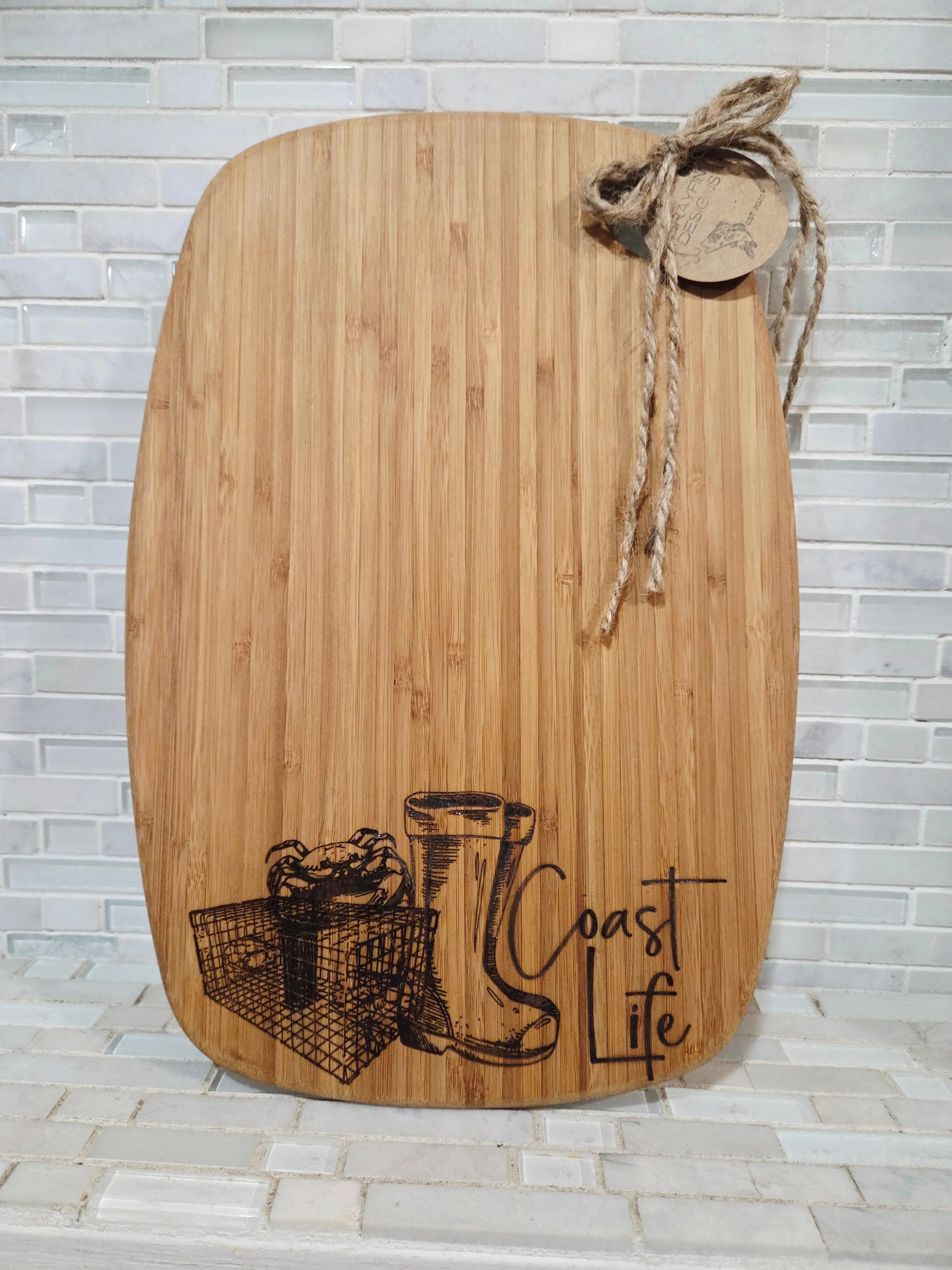 Bamboo cutting board with \"Coastal Life\" design, crab, and rain boots art from Main Street Collective.