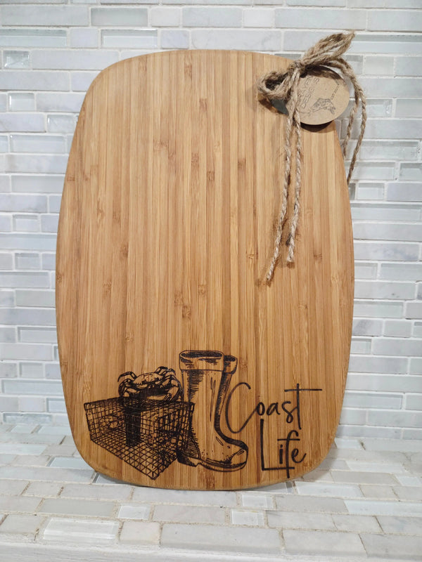 Bamboo cutting board with \"Coastal Life\" design, crab, and rain boots art from Main Street Collective.