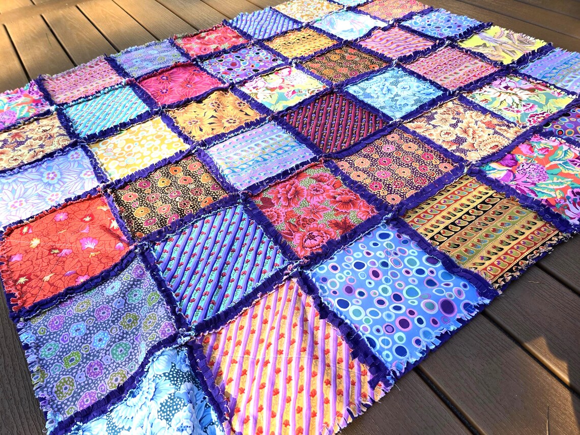 Colorful patchwork rag quilt with cotton squares and soft fleece backing. Handmade throw blanket on wood surface.
