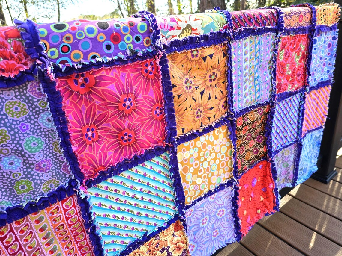 Colorful rag quilt: patchwork cotton squares with fleece backing. Handmade throw blanket with purple fringe.
