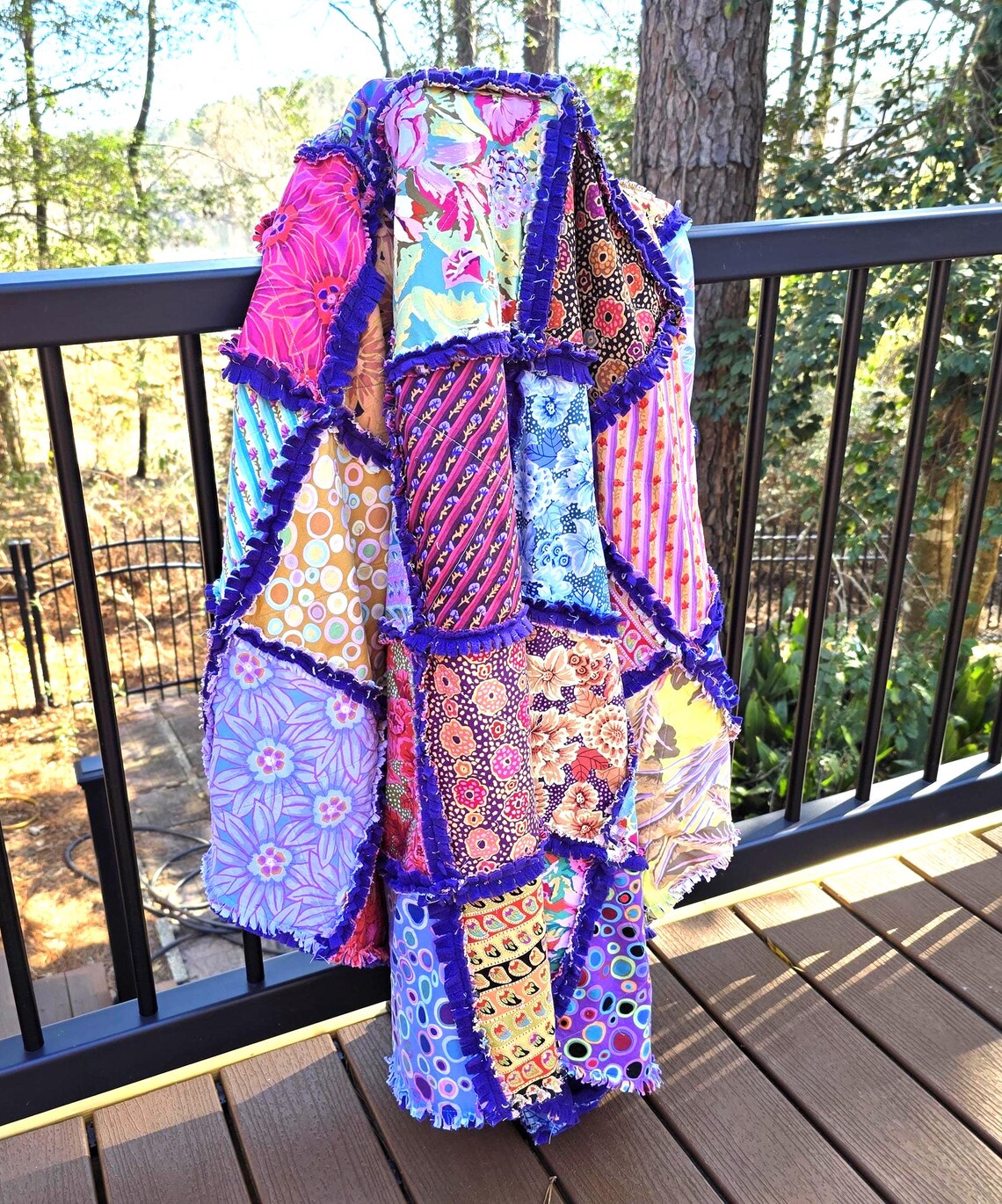 Colorful handmade rag quilt throw with cotton patchwork and blue fringe hanging on a deck railing.
