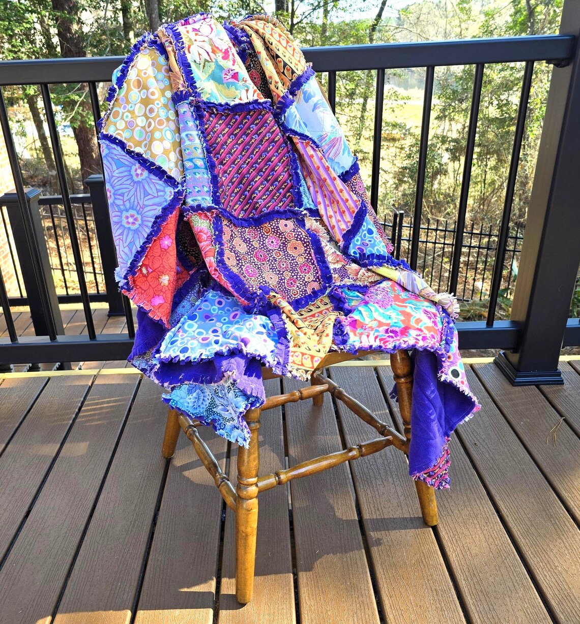 Colorful handmade rag quilt with patchwork squares and a soft fleece backing draped on a wooden chair on a deck.