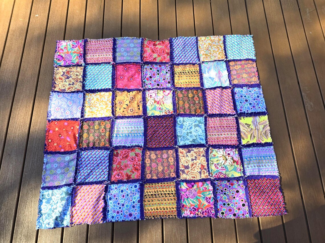 Patchwork rag quilt with colorful fabric squares and fleece backing on a wooden surface.