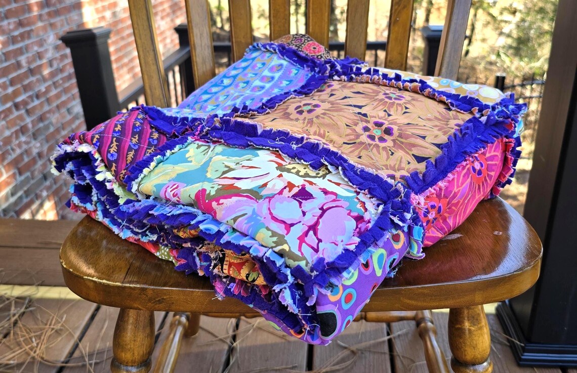 Colorful patchwork rag quilt with fleece backing on a wooden chair; cotton squares in floral, dot, and striped patterns.
