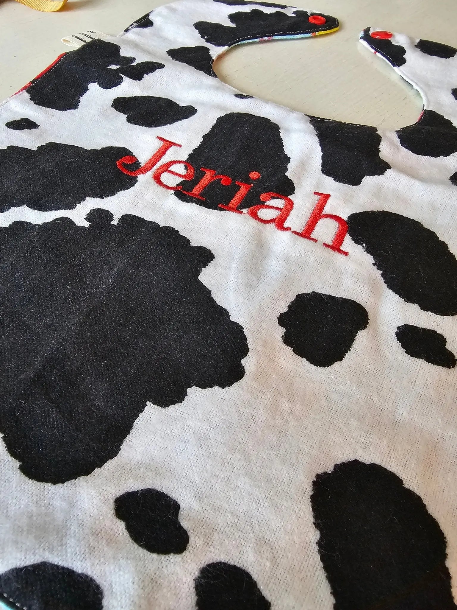 Personalized baby bib with cow print and embroidered name "Jeremiah". Handmade baby essential for feeding time.