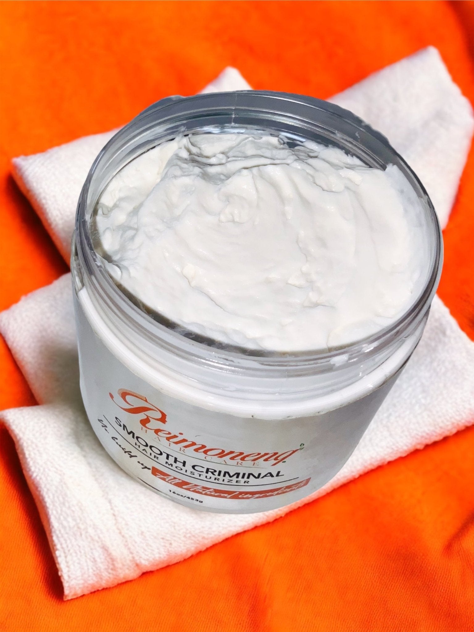 Reimoneng Smooth Criminal Hair Moisturizer jar on towel. All-natural hair care for moisture, detangling, and definition.