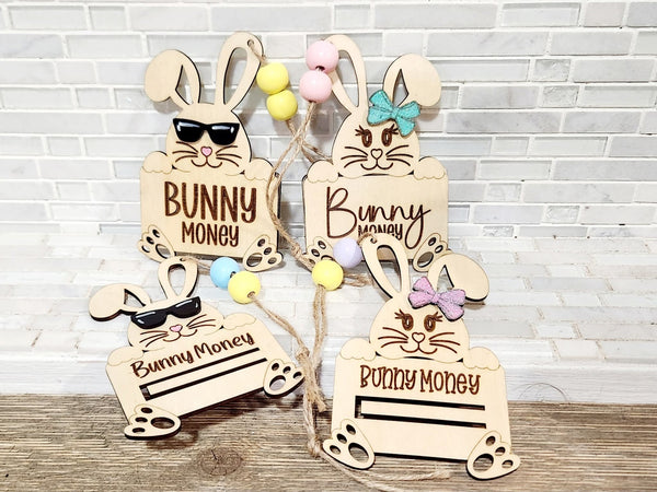 Four wooden Easter bunny money holders with sunglasses, bows, and bead accents against a brick background.