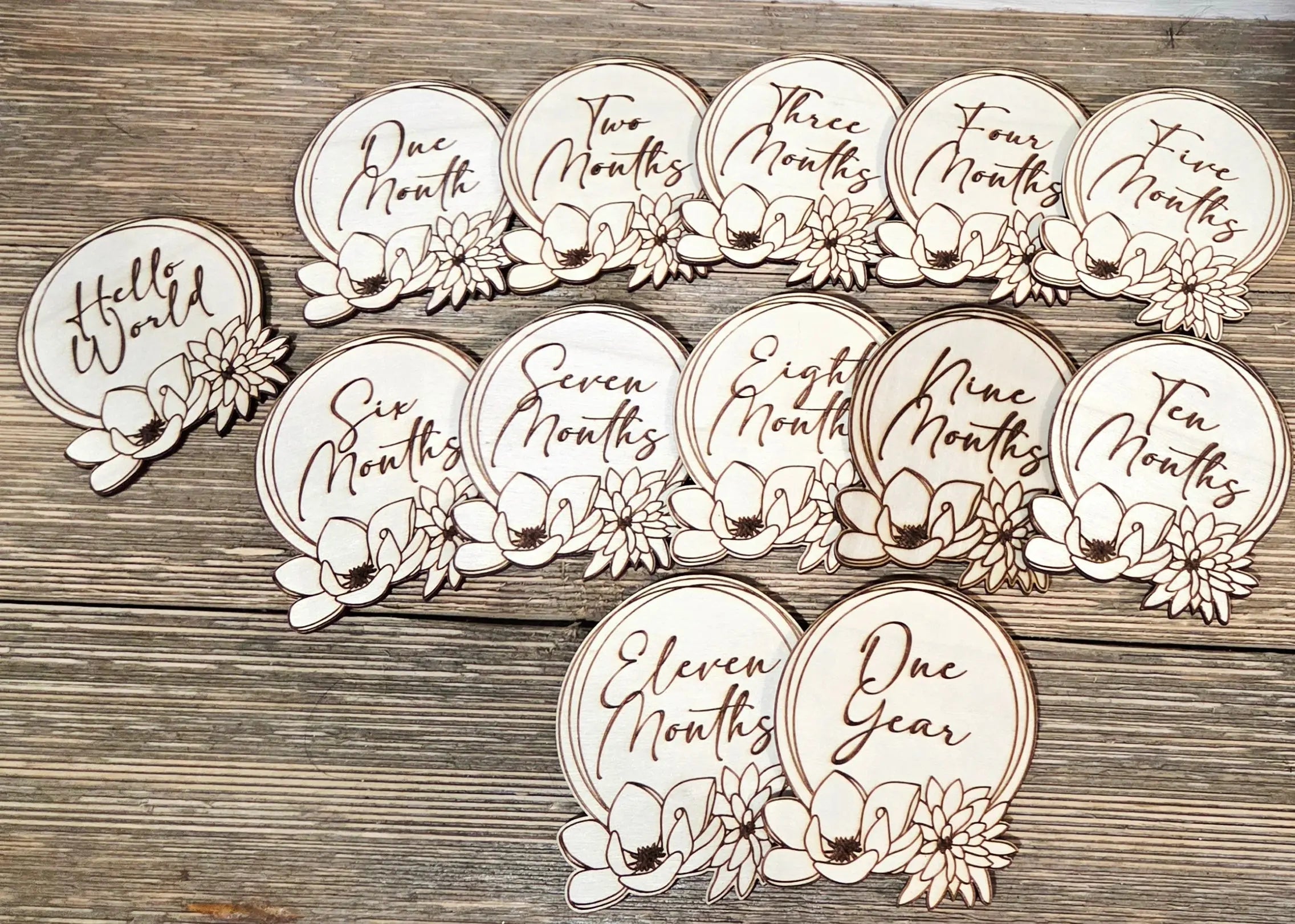 Wooden baby milestone discs featuring floral designs for monthly growth tracking, set on a wood background.