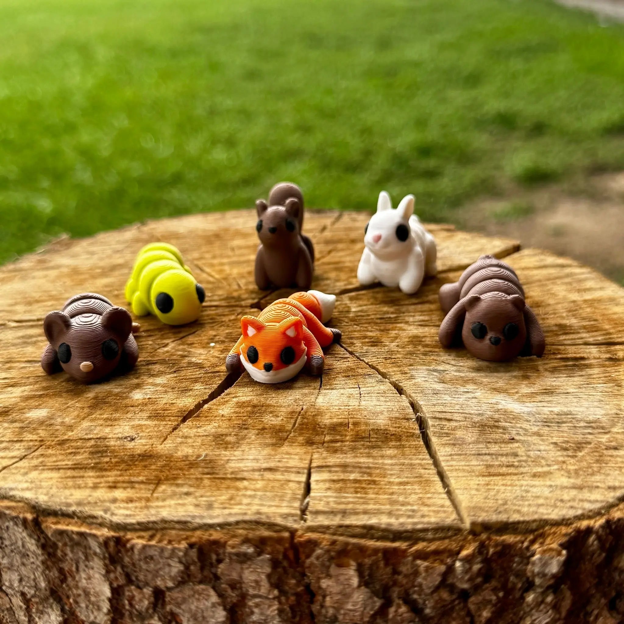 3D-printed woodland animal fidget toys: bear, fox, bunny, caterpillar, bumblebee, mouse on tree stump.
