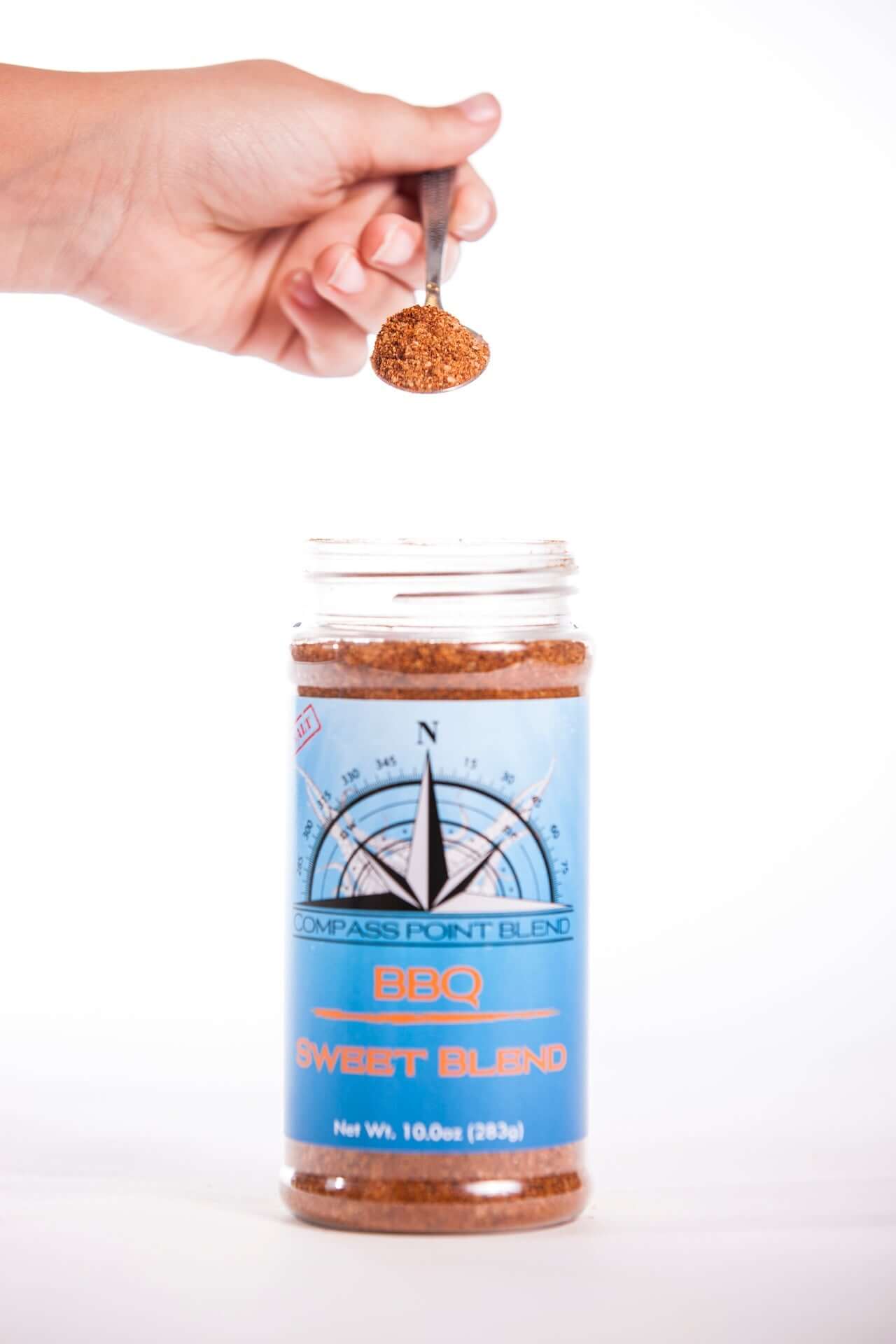 Hand holding a spoonful of Smoky Sweet BBQ Blend showing full jar and seasoning texture – Compass Point Blends