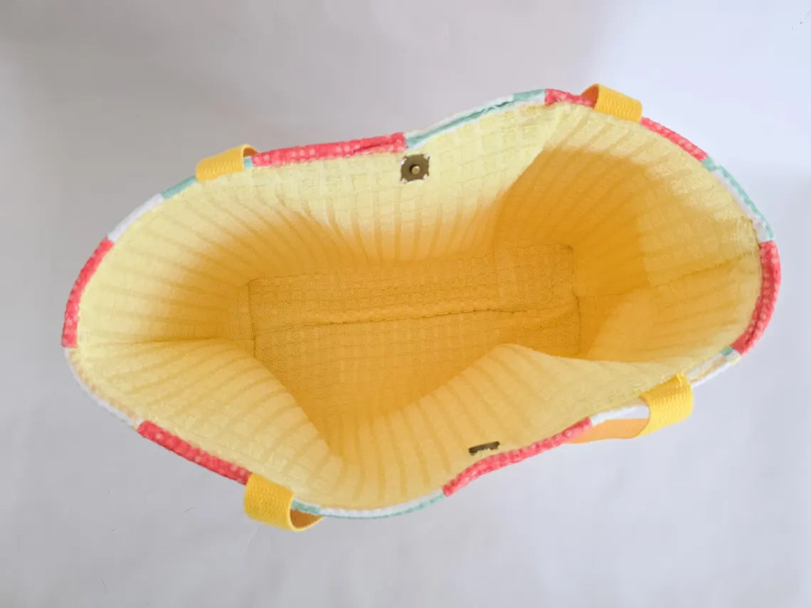 Open terry cloth beach tote with yellow straps. Striped exterior and yellow interior. Two magnetic clasps are visible.