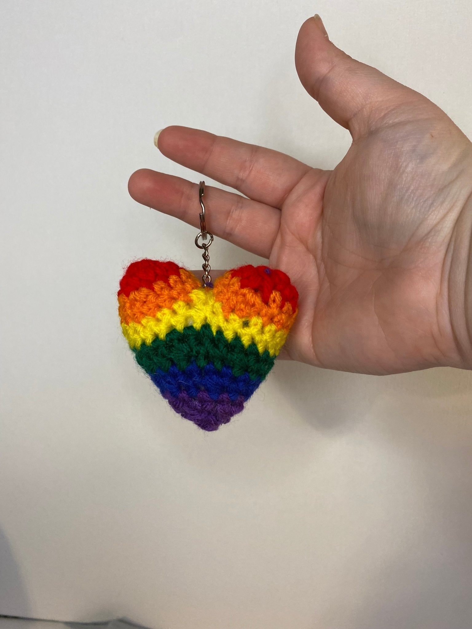 Handmade crocheted LGBTQ heart keychain with colorful pride flag yarn.