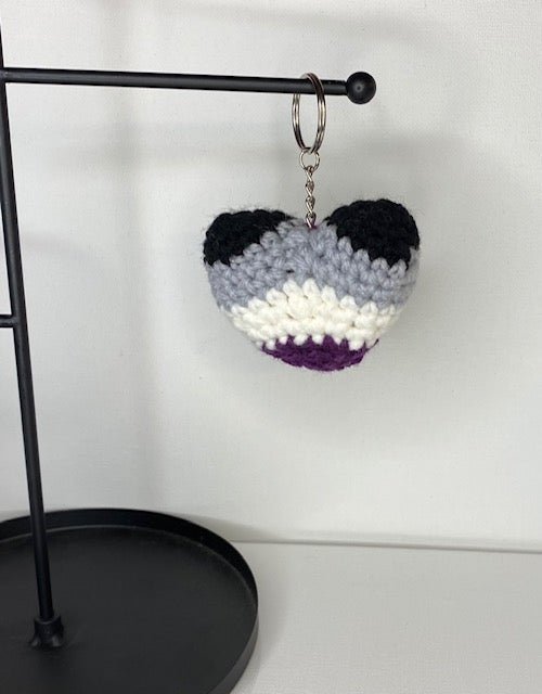 Handmade crocheted heart keychain in asexual pride colors: black, gray, white, and purple.