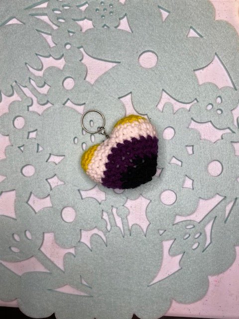 Handmade crocheted heart keychain in non-binary pride colors: yellow, white, purple, and black.