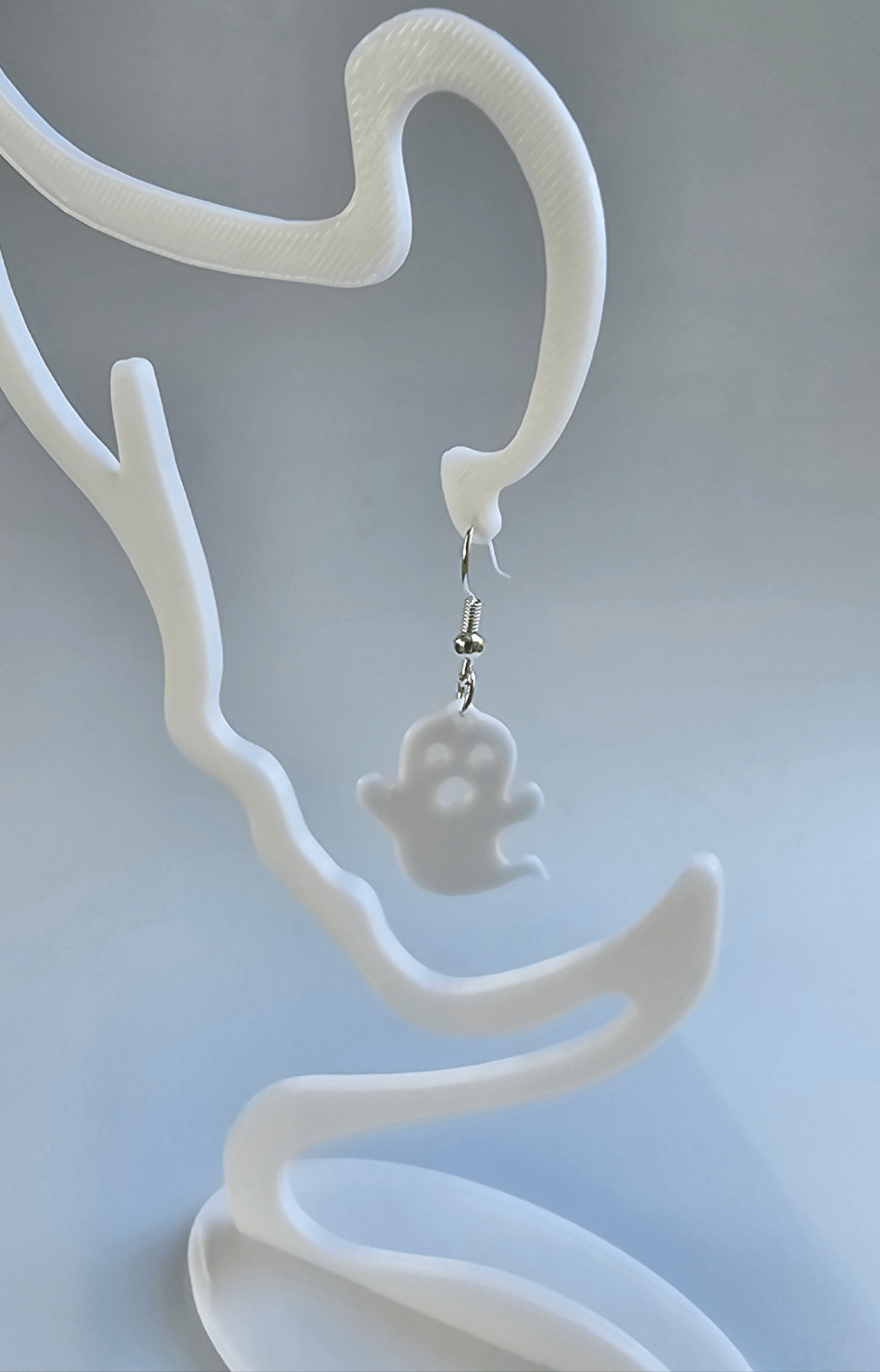 Ghost Earring Detail: White Ghost dangling from display. Handmade spooky Halloween earring by Main Street Collective teen artisan.