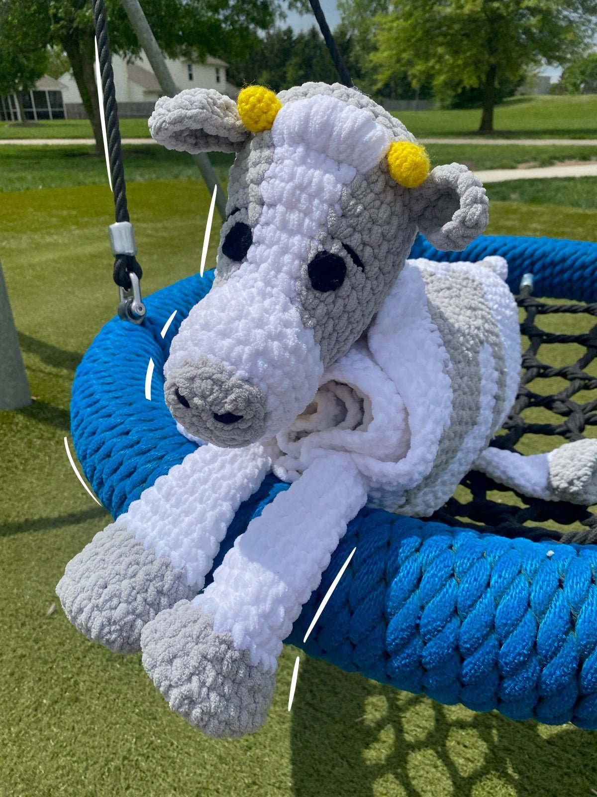Handmade crochet cow blanket on swing. Soft plush chenille yarn baby toy, perfect for nursery. Children and adult sizes available.