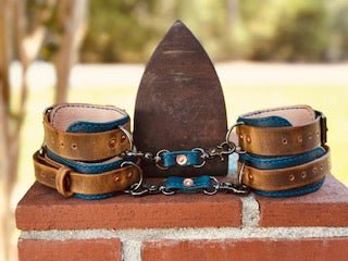 Leather wrist & ankle restraints set on brick with antique iron. Main Street Collective offering custom BDSM gear.