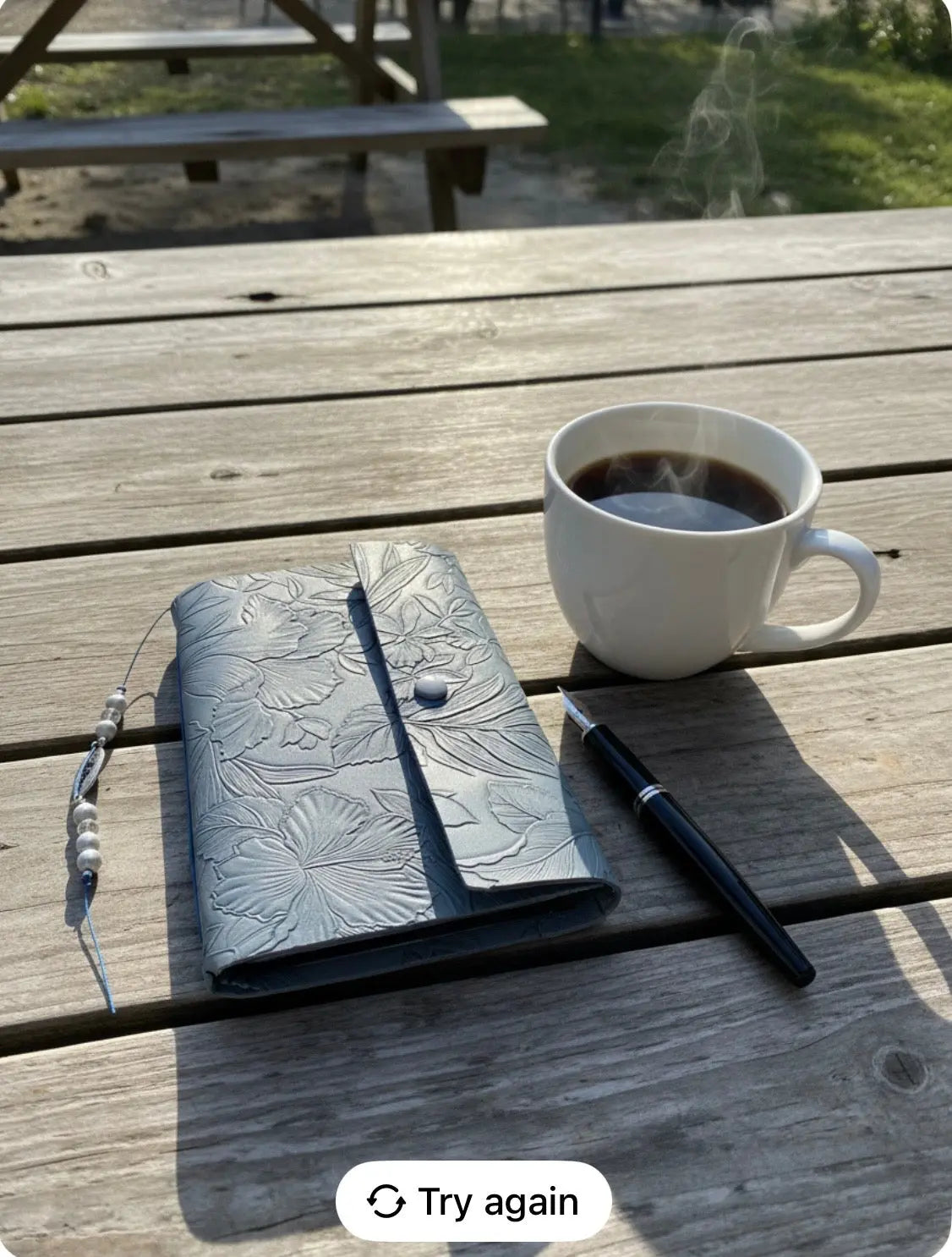 Floral embossed journal with a pen and steaming coffee cup on a weathered wooden table.