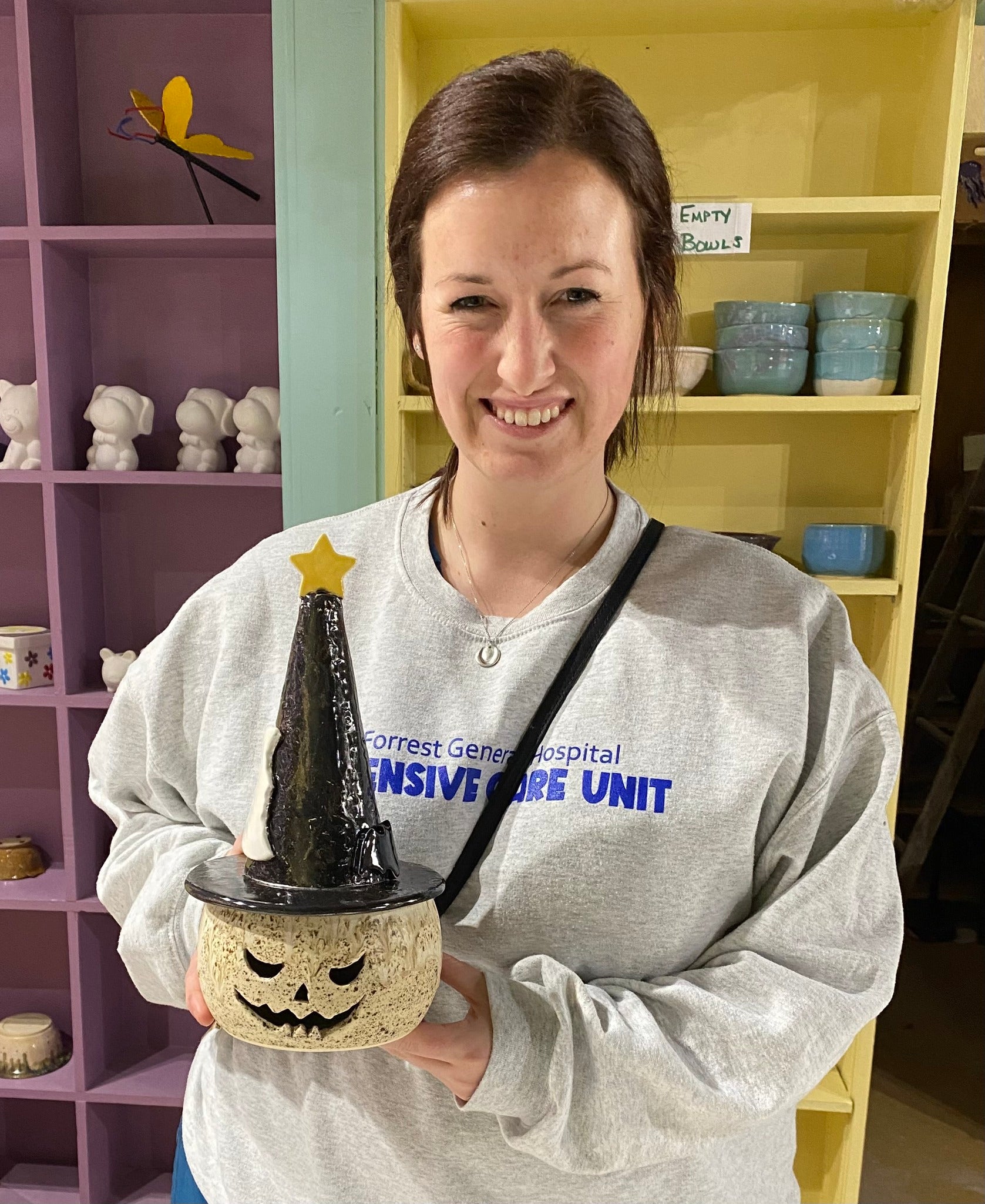 Woman holding Halloween pumpkin jack-o-lantern ceramic with witch hat at pottery studio. Handmade Halloween decor.