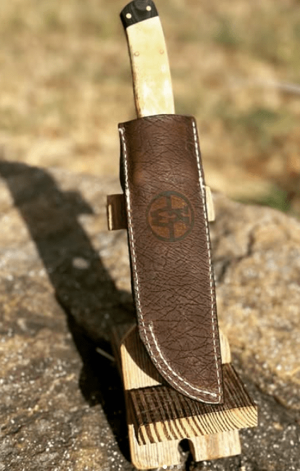 Handcrafted leather knife sheath with emblem detail, sturdy stitching, ideal for outdoor carry and everyday blade protection.