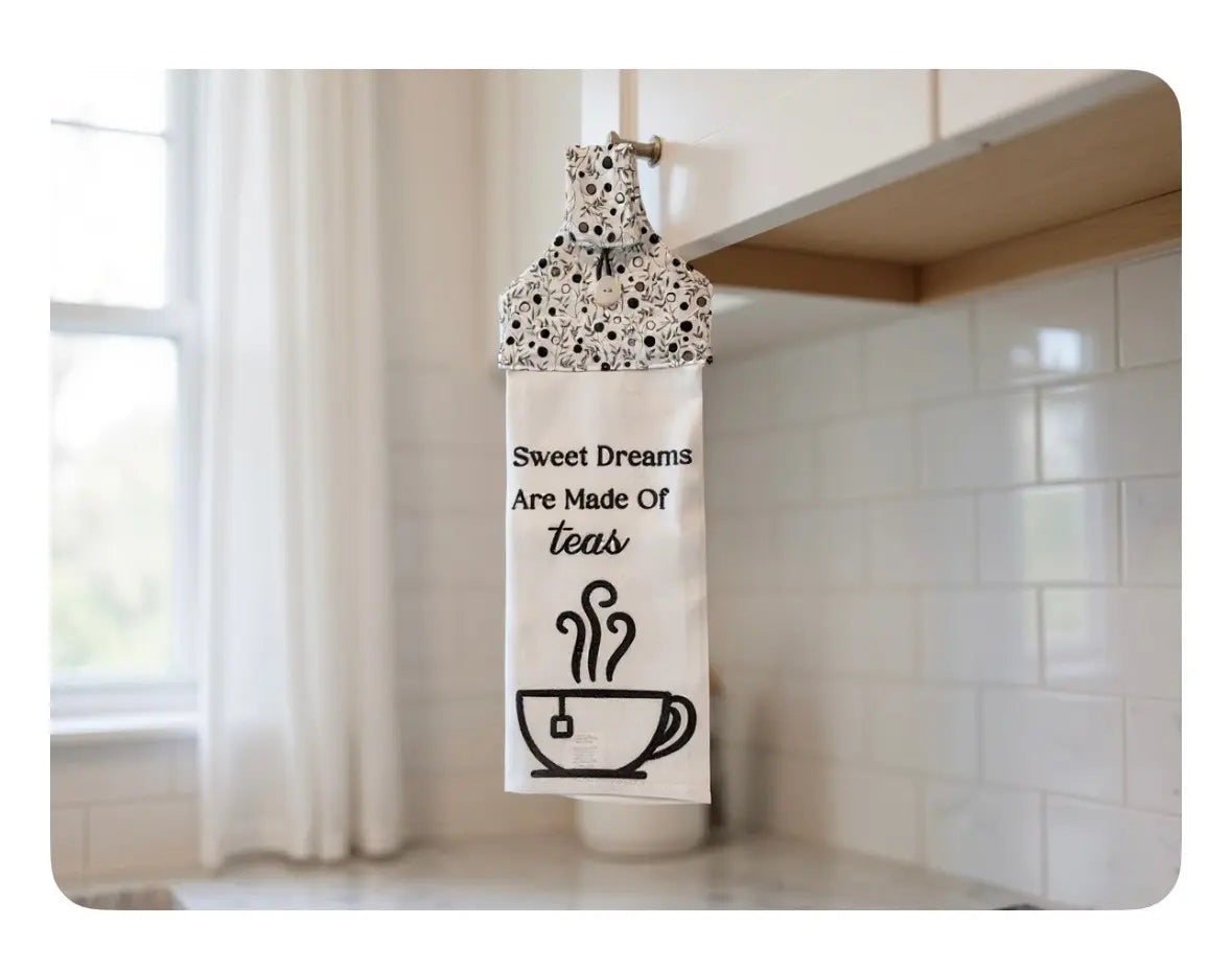 Tea towel with \"Sweet Dreams Are Made Of Teas\" design hanging in kitchen with a teacup graphic.