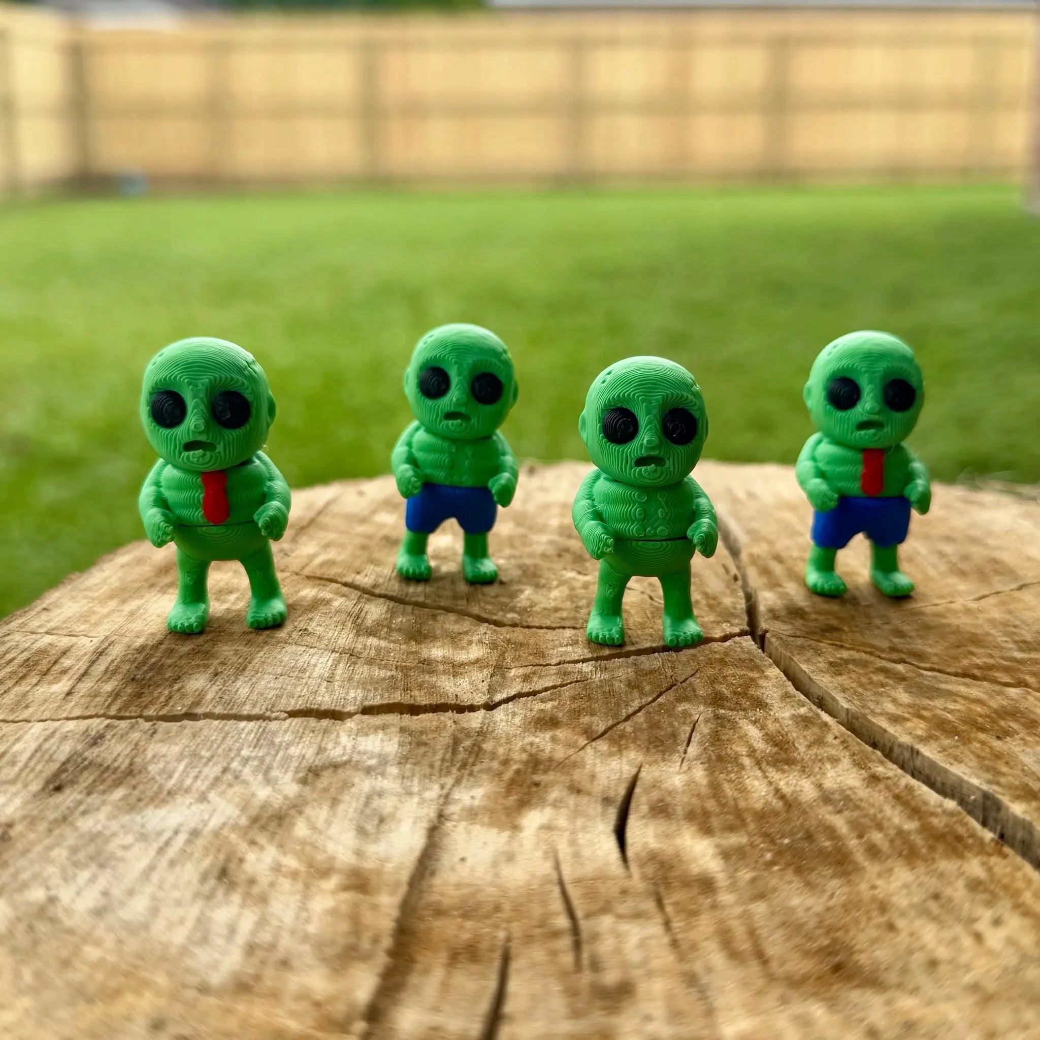 Four 3D printed zombie figures on a tree stump, Halloween theme, spooky toys.