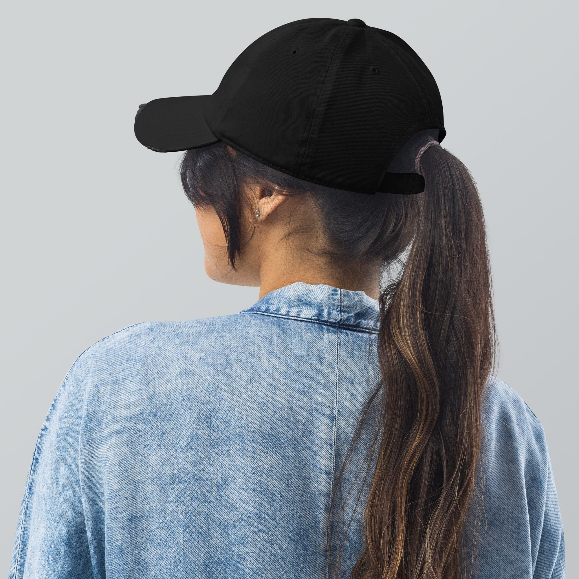 Woman wearing black cap, denim jacket, and ponytail. Back view.