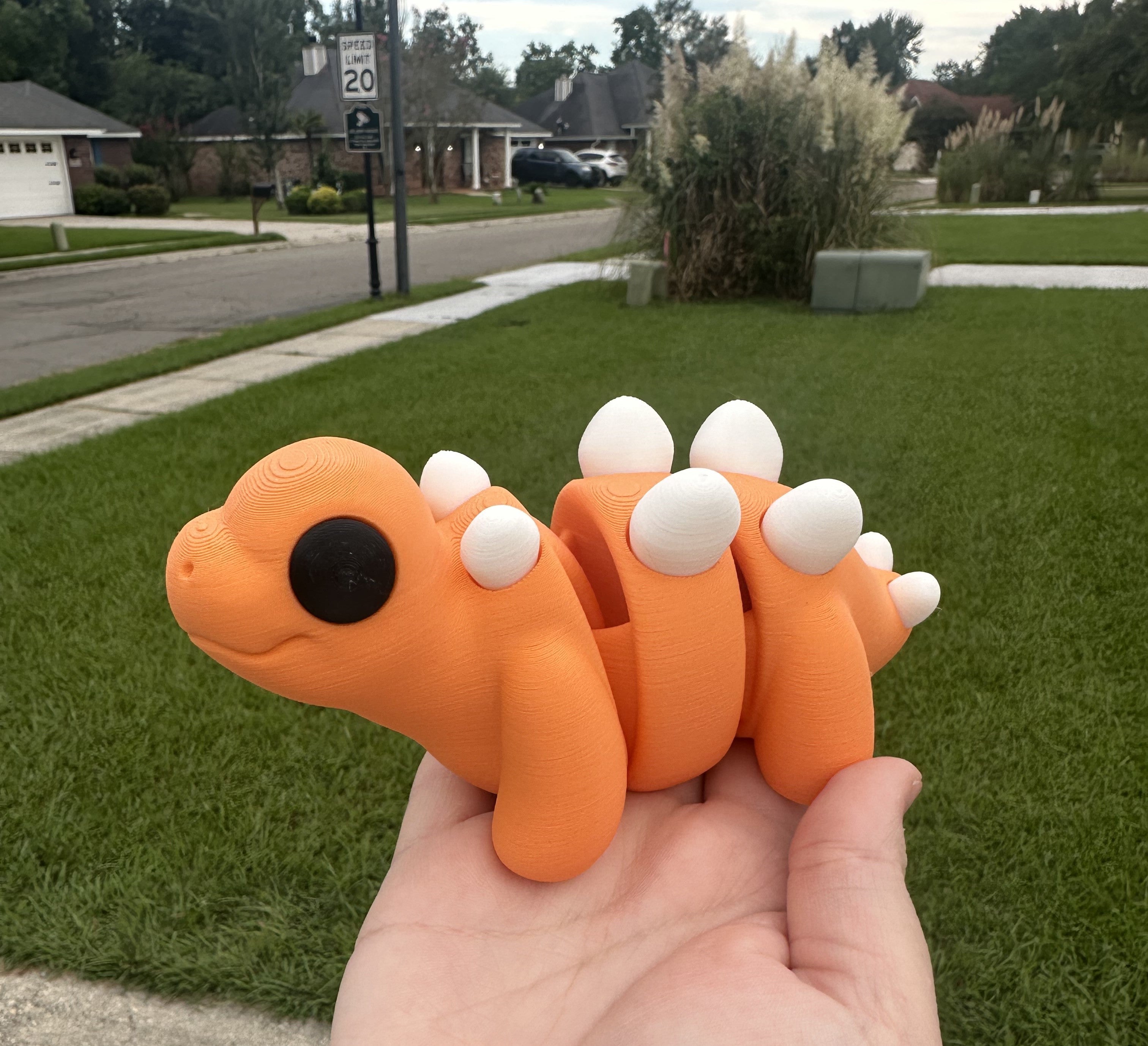 Orange 3D Printed Stegosaurus Fidget Toy (Large) held in hand outdoors by Main Street Collective. Movable segments, stress relief toy