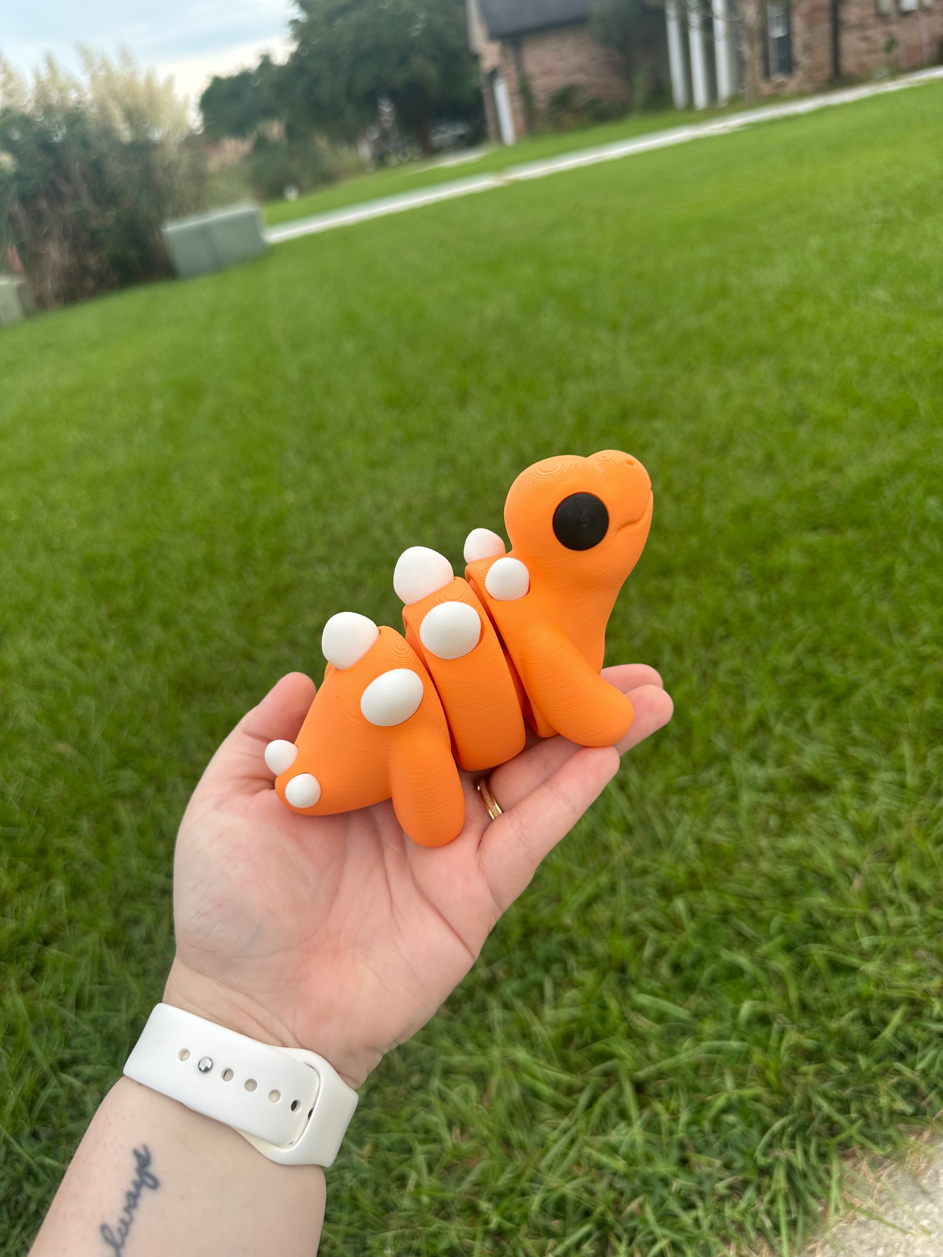 Orange 3D Printed Stegosaurus Fidget Toy on Hand with Green Grass Background - Main Street Collective