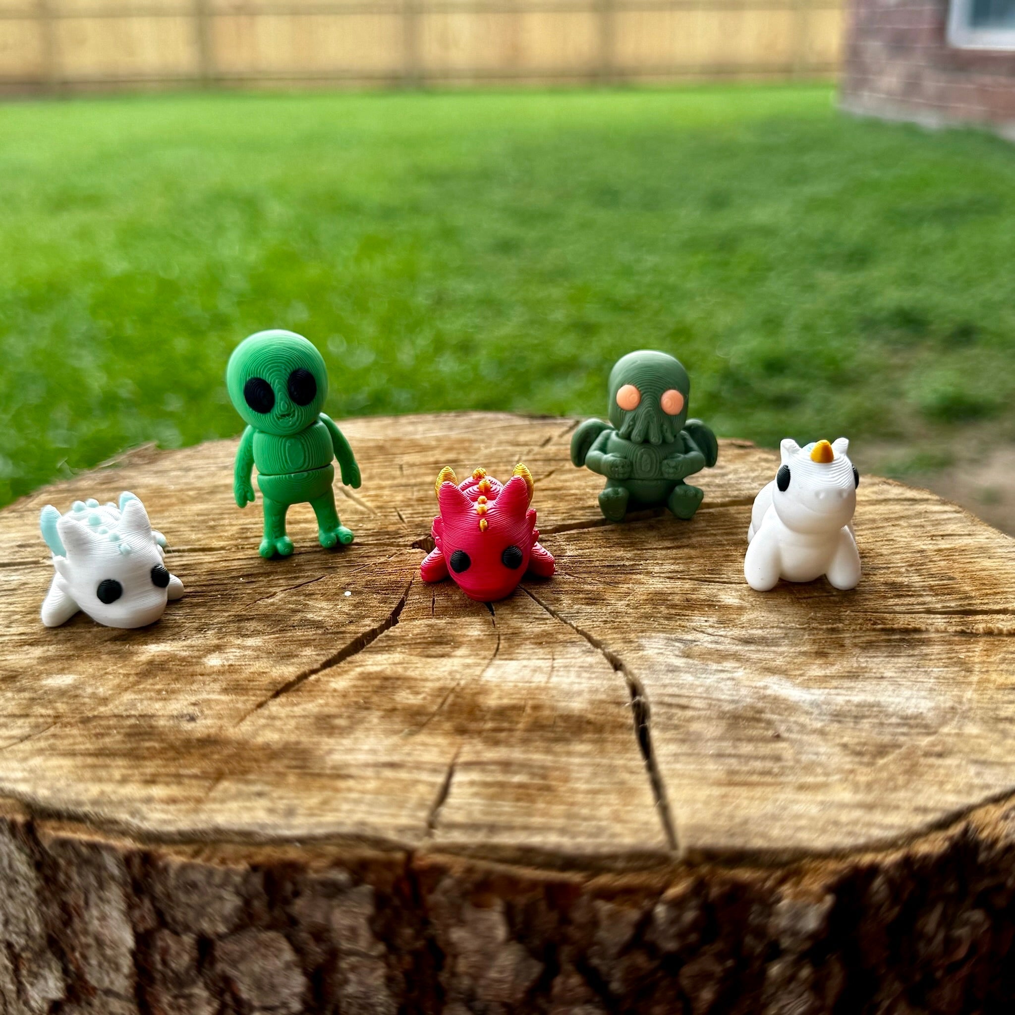 Fantasy Friends Mini Fidget Bundle: 3D printed alien, Cthulhu, dragon, & unicorn toys on tree stump, available at Main Street Collective.