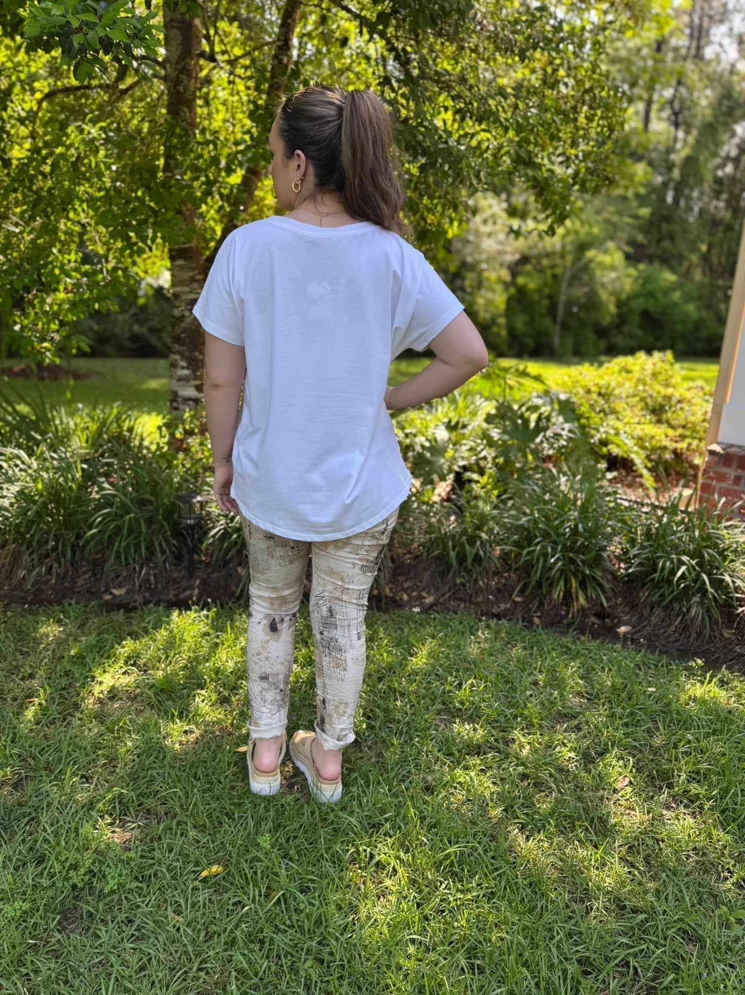 Woman in white Champagne Problems Italian tee, Main Street Collective boutique top in garden setting. Stylish and trendy fashion.
