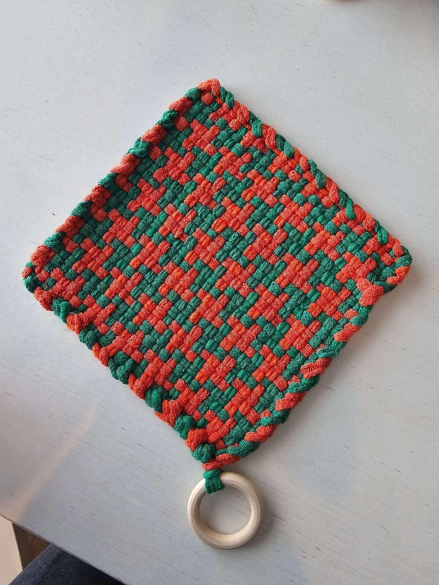 Handmade woven potholder, green and orange checkered design, kitchen accessory with wooden hanging ring.