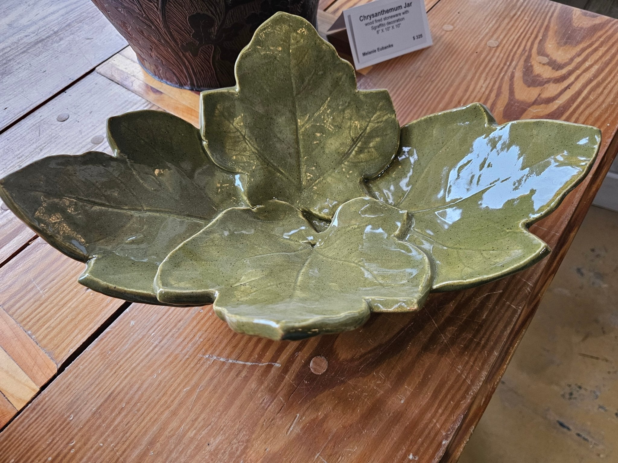 Green ceramic leaf bowl on wood. Handmade decorative pottery. Elegant leaf-shaped serving dish.