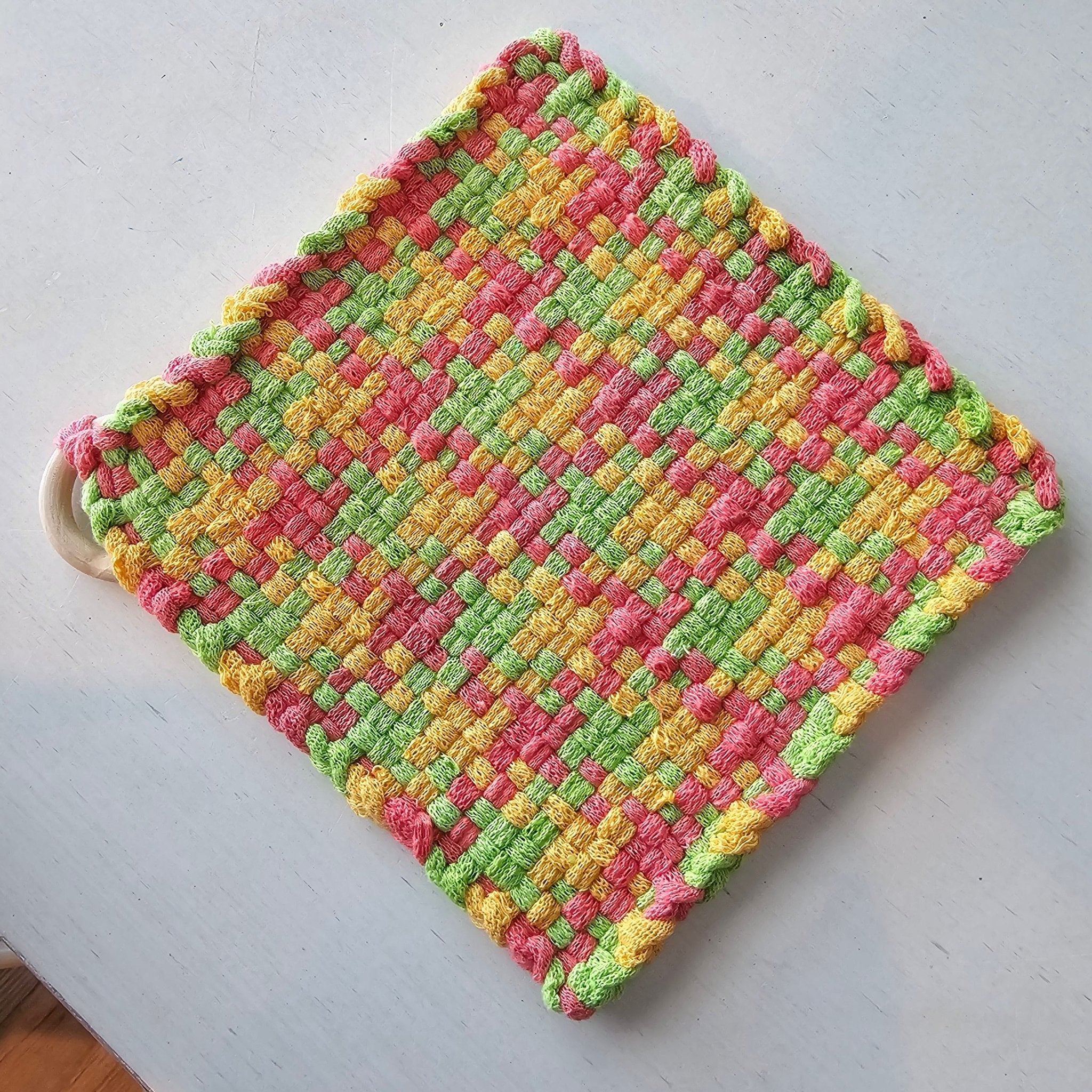 Handmade woven potholder with colorful pink, yellow, and green cotton loops by Penelope at Main Street Collective.